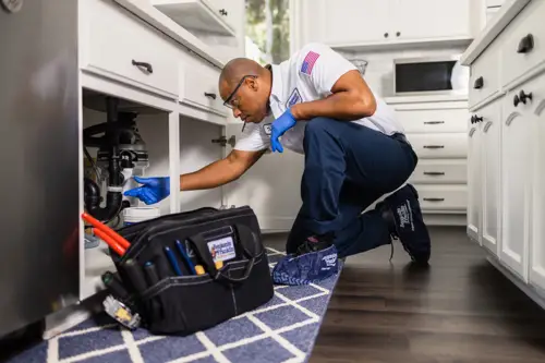 Benjamin Franklin Plumbing Tech, Trevor, working under a sink of a Niceville FL home