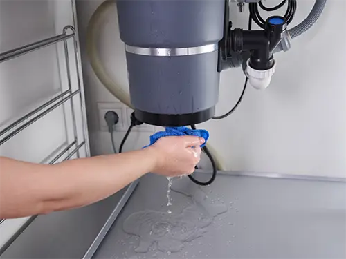 A garbage disposal leaking as a Benjamin Franklin Plumbing Tech works on it