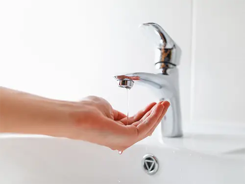 A Niceville FL homeowner's hand showing low water pressure from a sink faucet in her bathroom